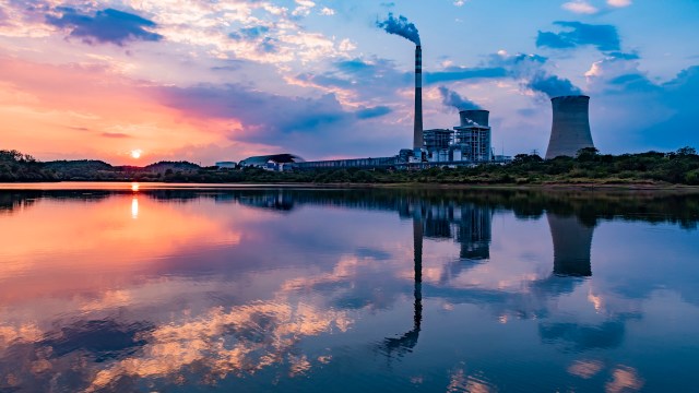 A nuclear power plant with cooling towers reflects in a lake at sunset.