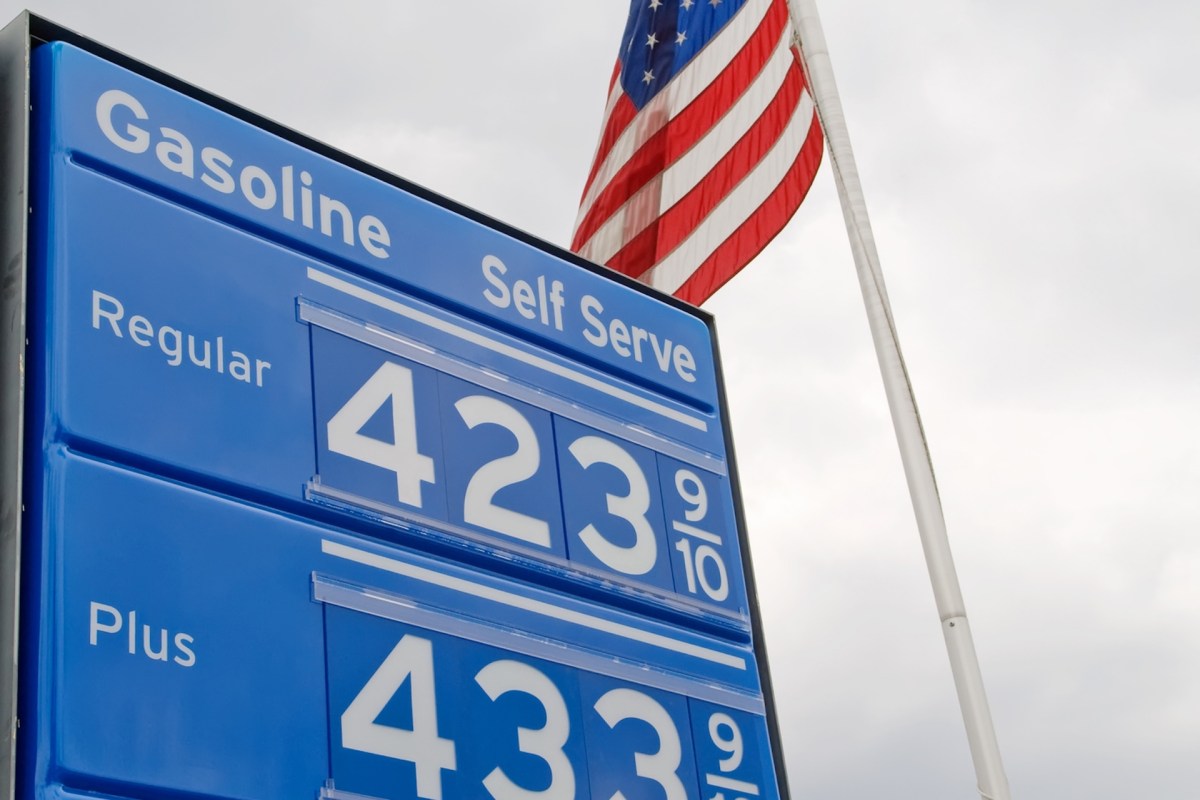 A gas station sign displays gasoline prices: Regular at $4.23 and Plus at $4.33, with an American flag in the background.