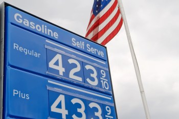 A gas station sign displays gasoline prices: Regular at $4.23 and Plus at $4.33, with an American flag in the background.