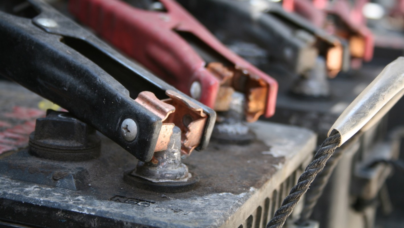 Close-up of battery terminals with red and black jumper cables connected.