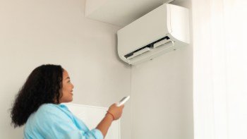 A person using a remote control to operate a wall-mounted air conditioner in a well-lit room.