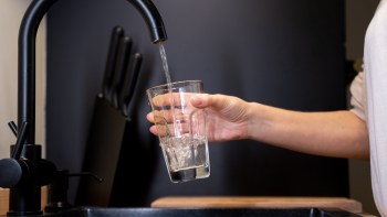 A person fills a clear glass with water from a modern black kitchen faucet.