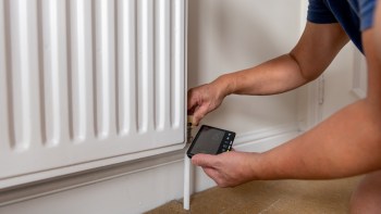 A person using a device to adjust the settings on a radiator valve in a home.