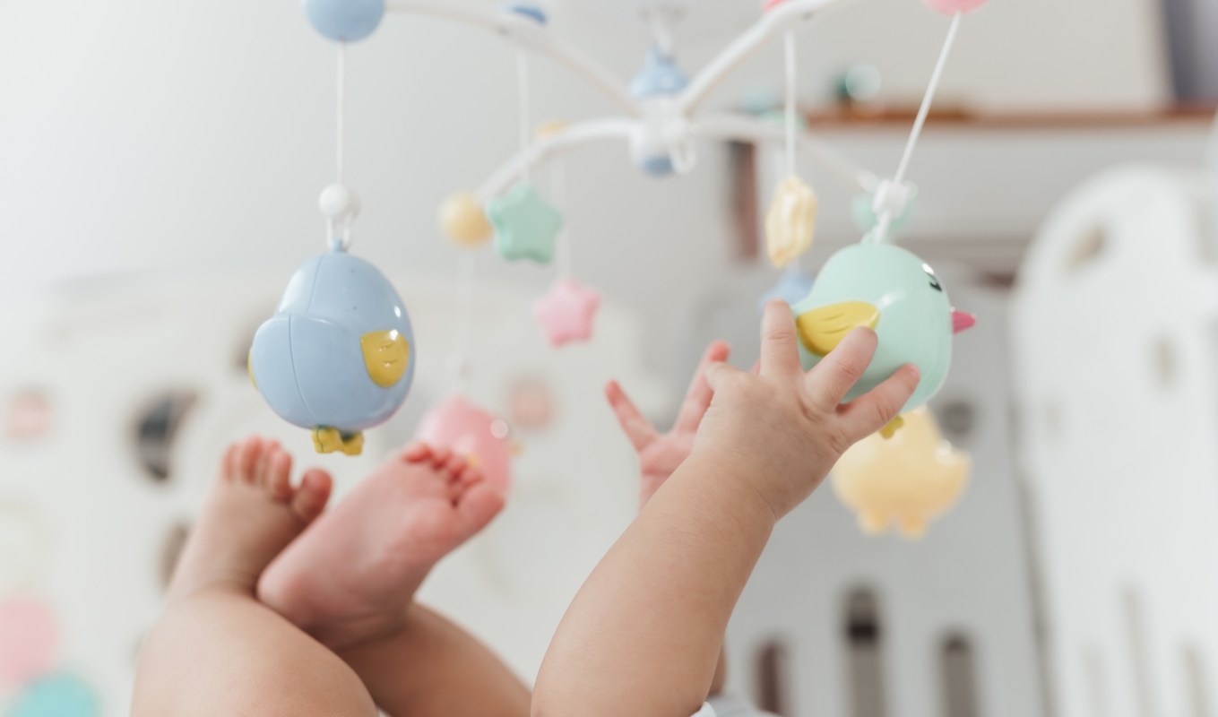 A baby reaching for colorful hanging toys in a bright nursery.