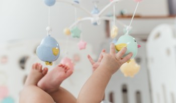 A baby reaching for colorful hanging toys in a bright nursery.