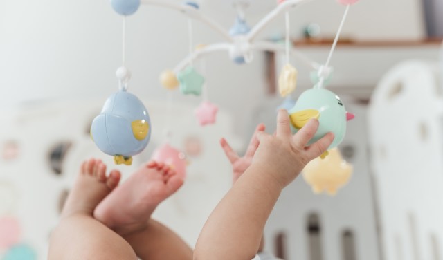 A baby reaching for colorful hanging toys in a bright nursery.