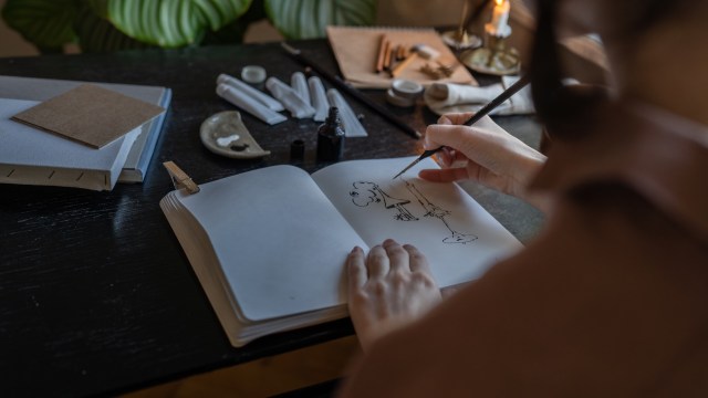 A person hand inking a cartoon in a sketchbook.