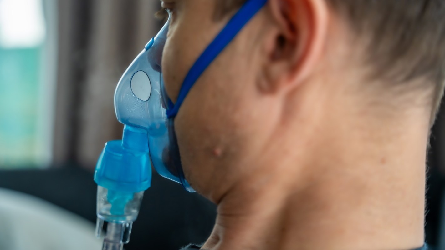 A close-up of a person using a blue nebulizer mask for respiratory treatment.