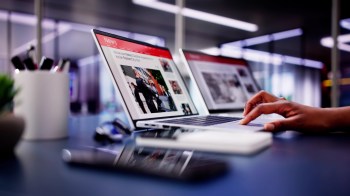 A person uses a laptop to read the news in an office.