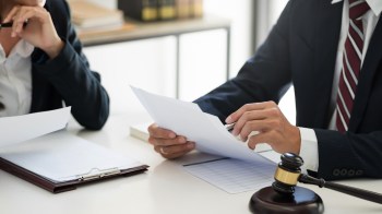 A lawyer discussing documents with a client at a desk, featuring a gavel and law books in the background.