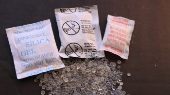 Three desiccant packets labeled "Silica Gel" and "Mineral Desiccant" are shown on a black surface with scattered gel beads.