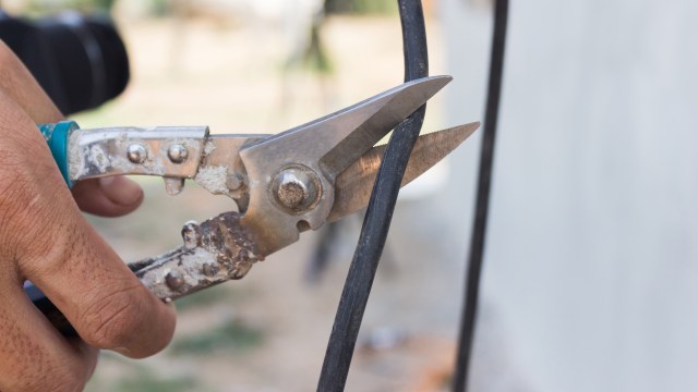 A person using a wirecutter to cut a thick black cable.