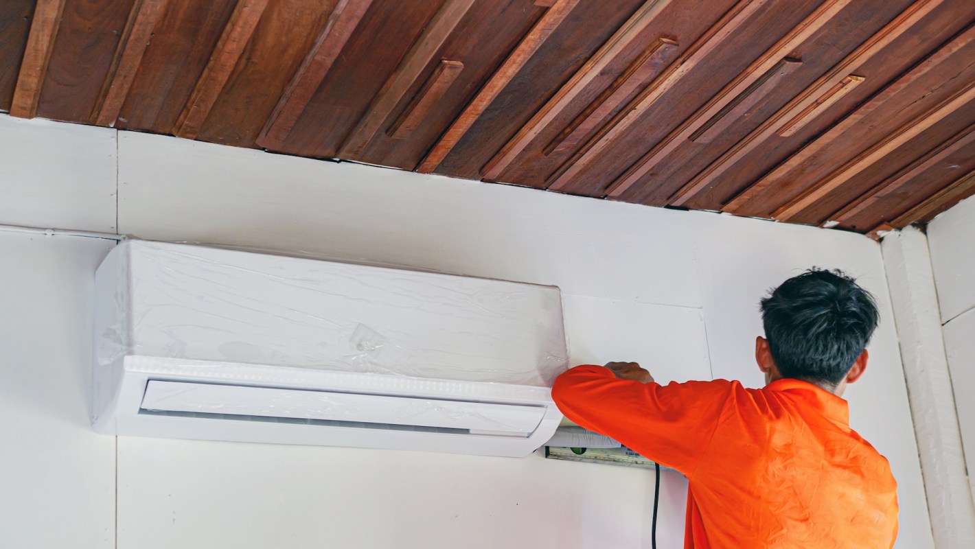 A technician installs a heat pump unit on a wall.