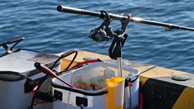 A fishing rod and tackle box are set on the edge of a dock over water, with tools and bait containers nearby.