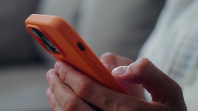 A close-up of a person's hands holding an orange smartphone while navigating the screen.
