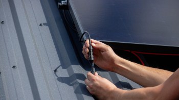 A person connects a cable to a solar panel on a metal roof.