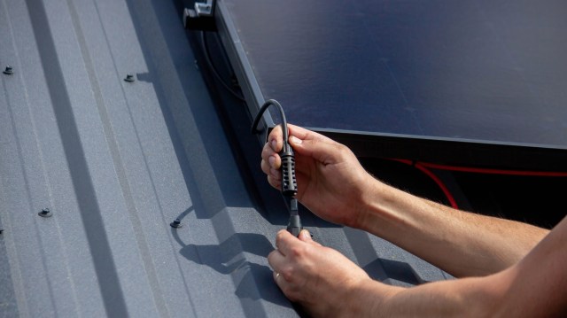 A person connects a cable to a solar panel on a metal roof.