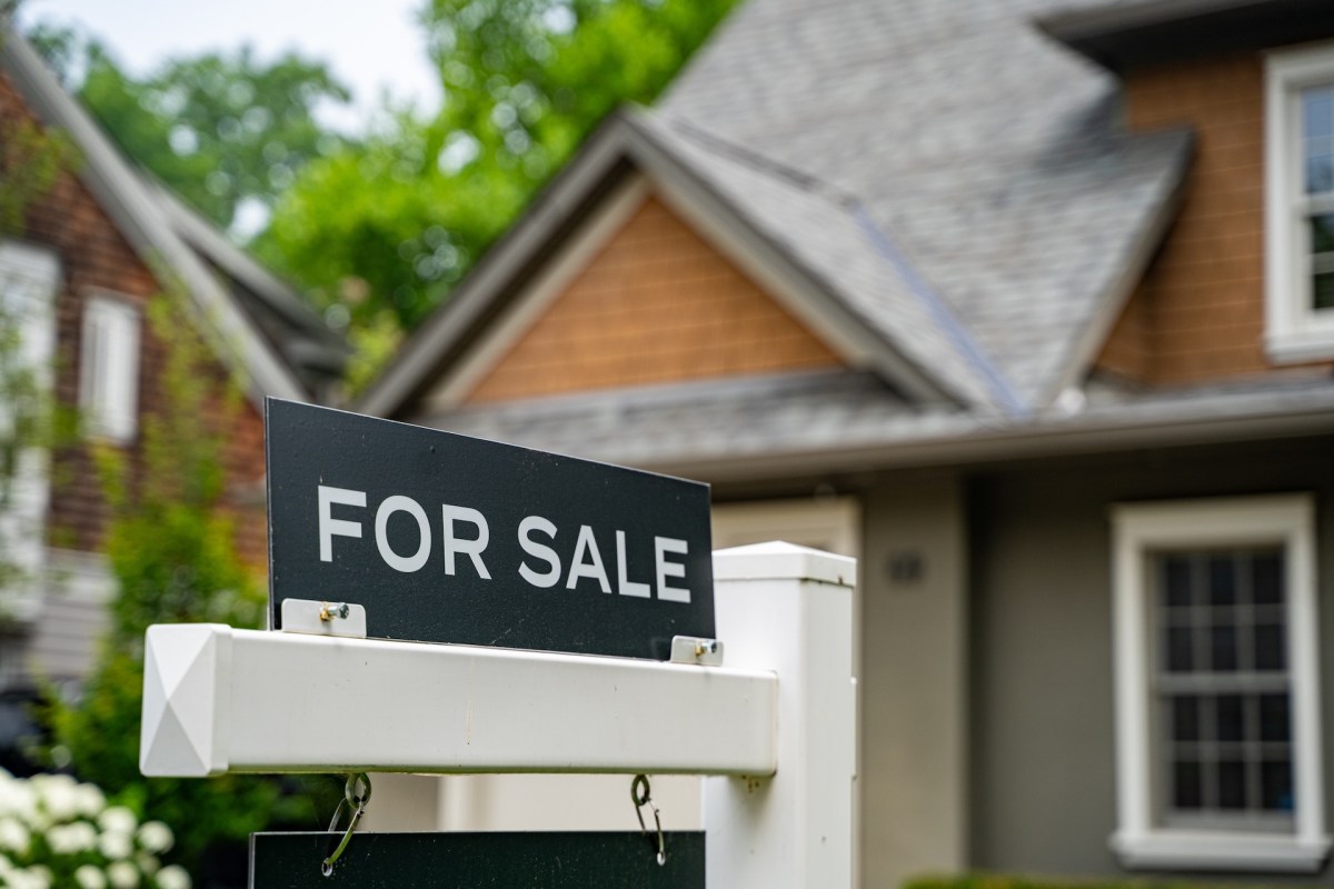 A close-up of a black "For Sale" sign in front of a residential house.