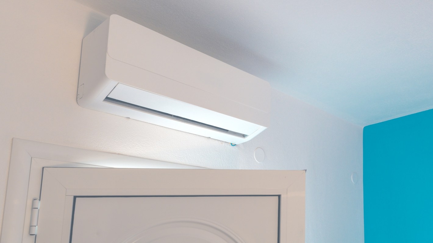 A modern, white air conditioner mounted on a wall above a door in an apartment.
