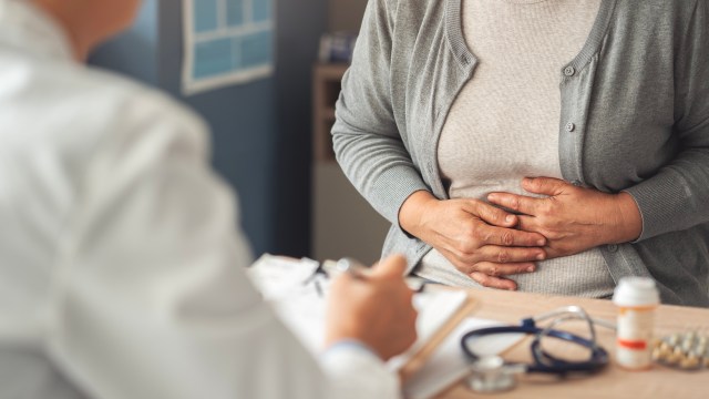 A patient holds their stomach while discussing symptoms with a doctor in a medical office.