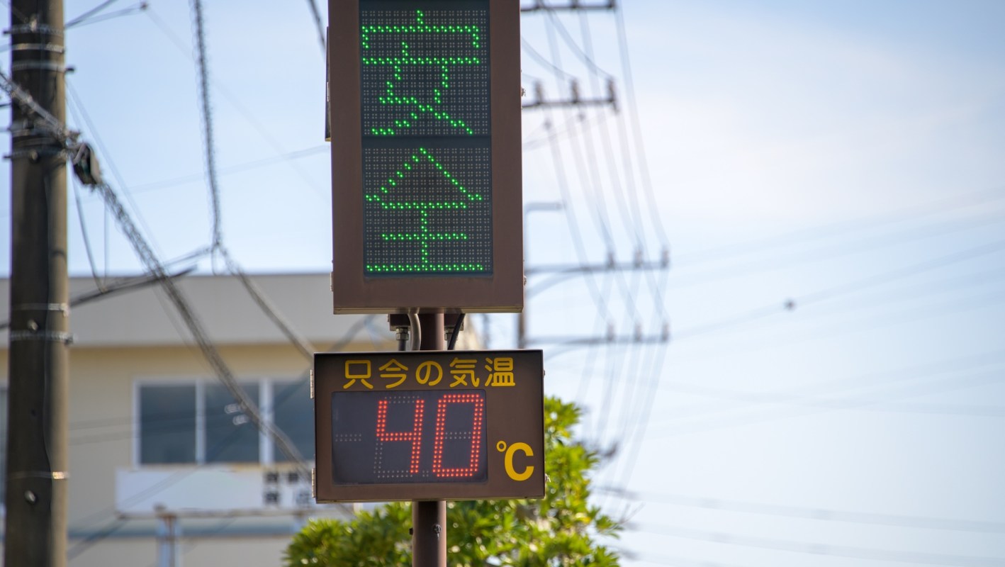 A digital temperature display shows 40 degrees Celsius with green safety signals in Japanese above it against a bright sky.