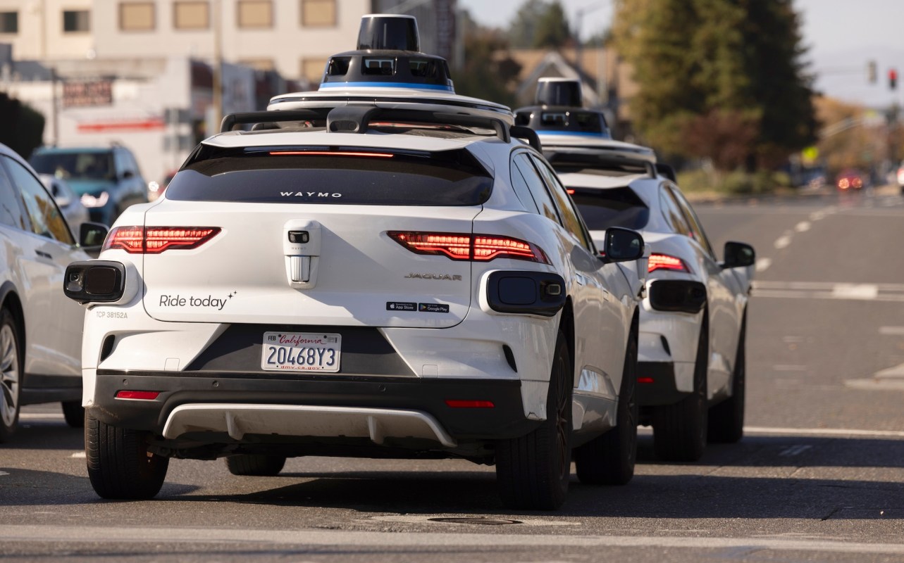 Two white autonomous vehicles from Waymo are stopped at an intersection, showcasing their distinct branding and sensors.