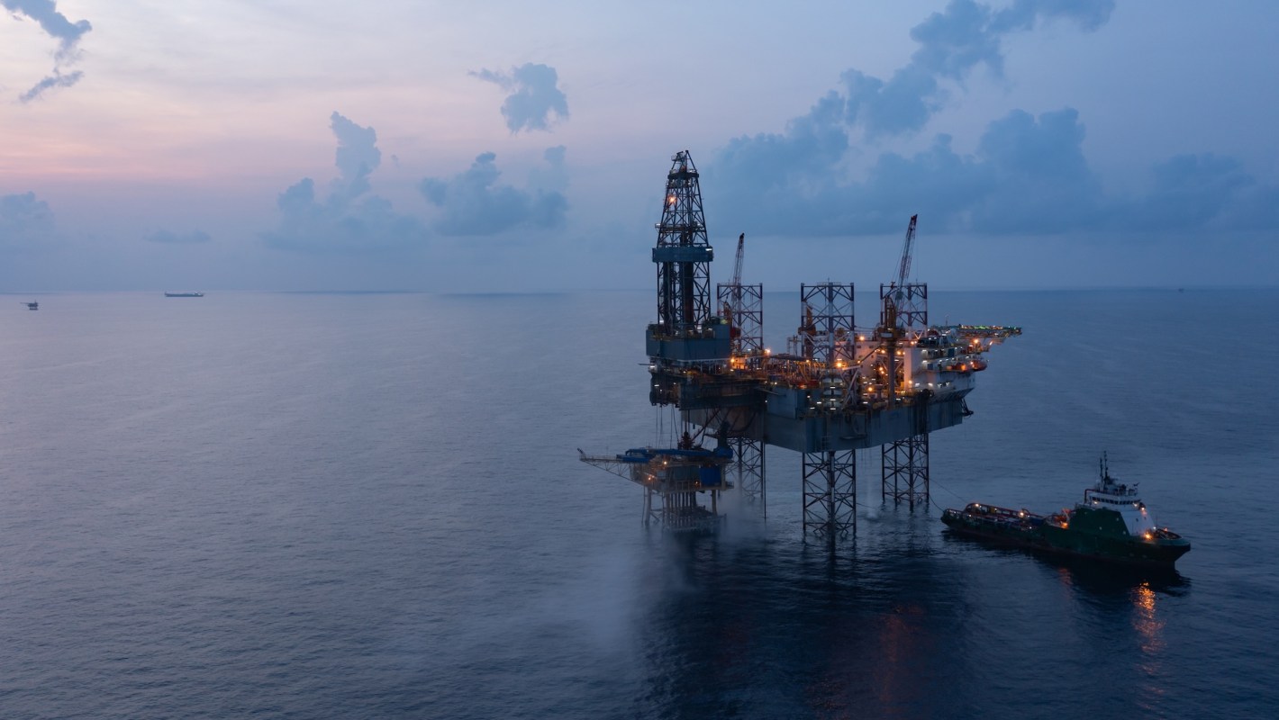 An offshore oil rig at dusk with a ship nearby.