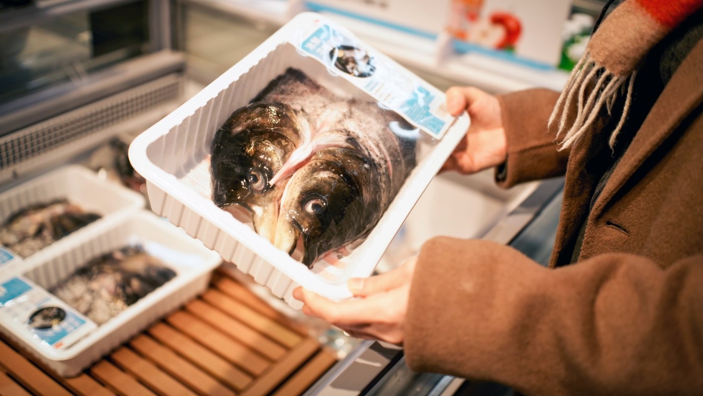 A person holding a tray of fish with visible heads in a seafood display case.