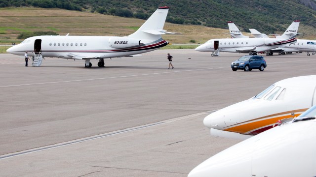 Several private jets parked at an airport with a car driving nearby and a person walking toward one of the planes.