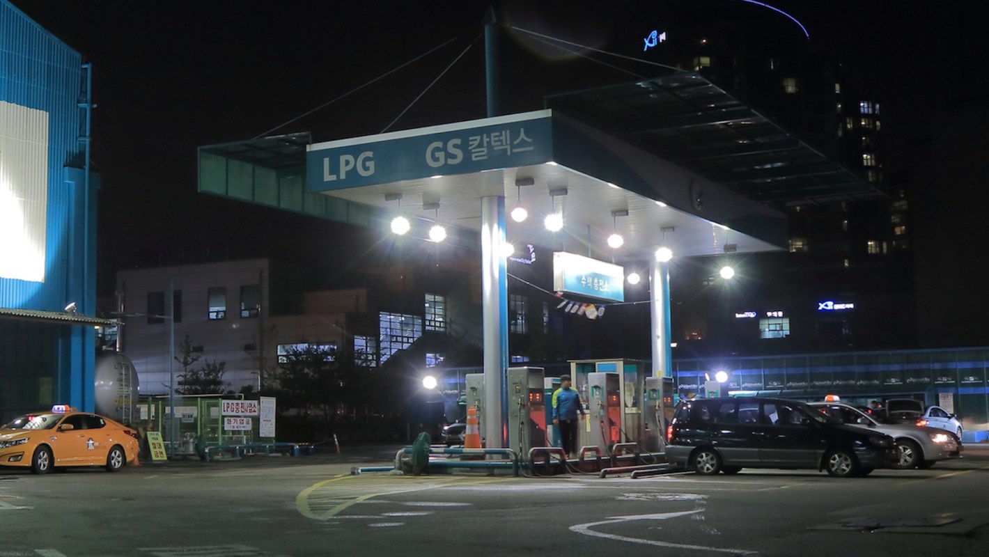 A nighttime view of an LPG gas station in South Korea with several cars and brightly lit fuel pumps.