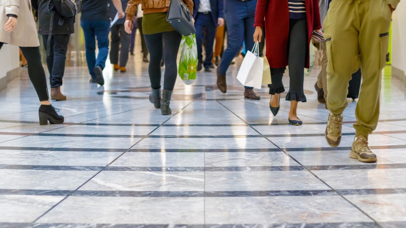 A bustling shopping mall scene with multiple people walking on a marble floor.