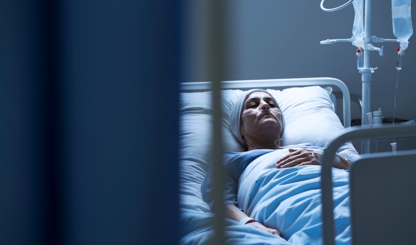 A woman lies in a hospital bed amid dark surroundings.