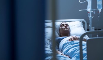 A woman lies in a hospital bed amid dark surroundings.