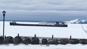 A large cargo ship navigates through a frozen lake under a cloudy sky.