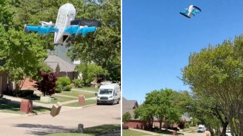 A drone delivers a package over a suburban street lined with trees and houses.