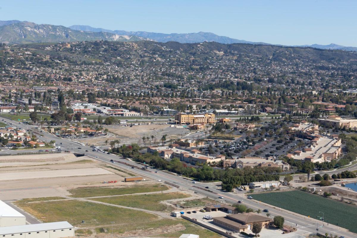 Aerial view of a California industrial site with highways, buildings, and mountains in the background.