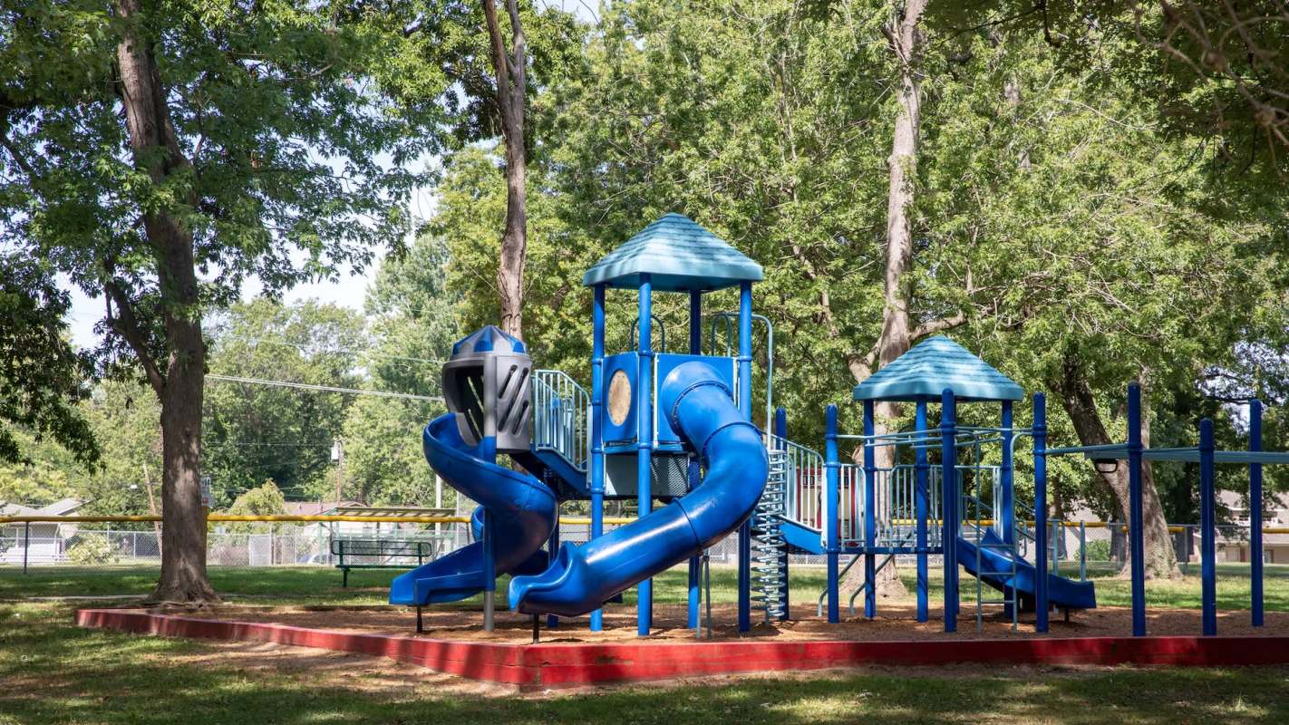 A colorful blue playground structure with slides and towers surrounded by trees in a park.
