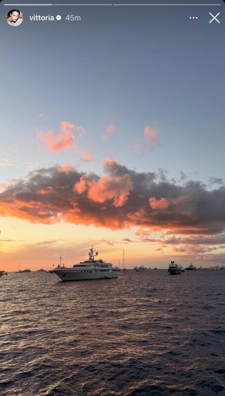 A yacht is in the water, with the sun setting in the background. 