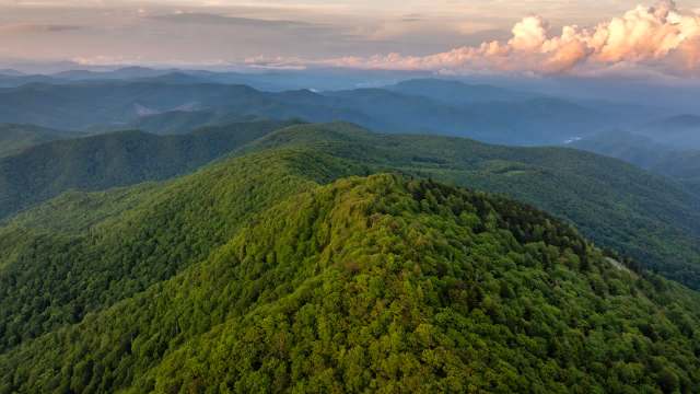 A sprawling landscape of lush green mountains under a cloudy sky at sunset.