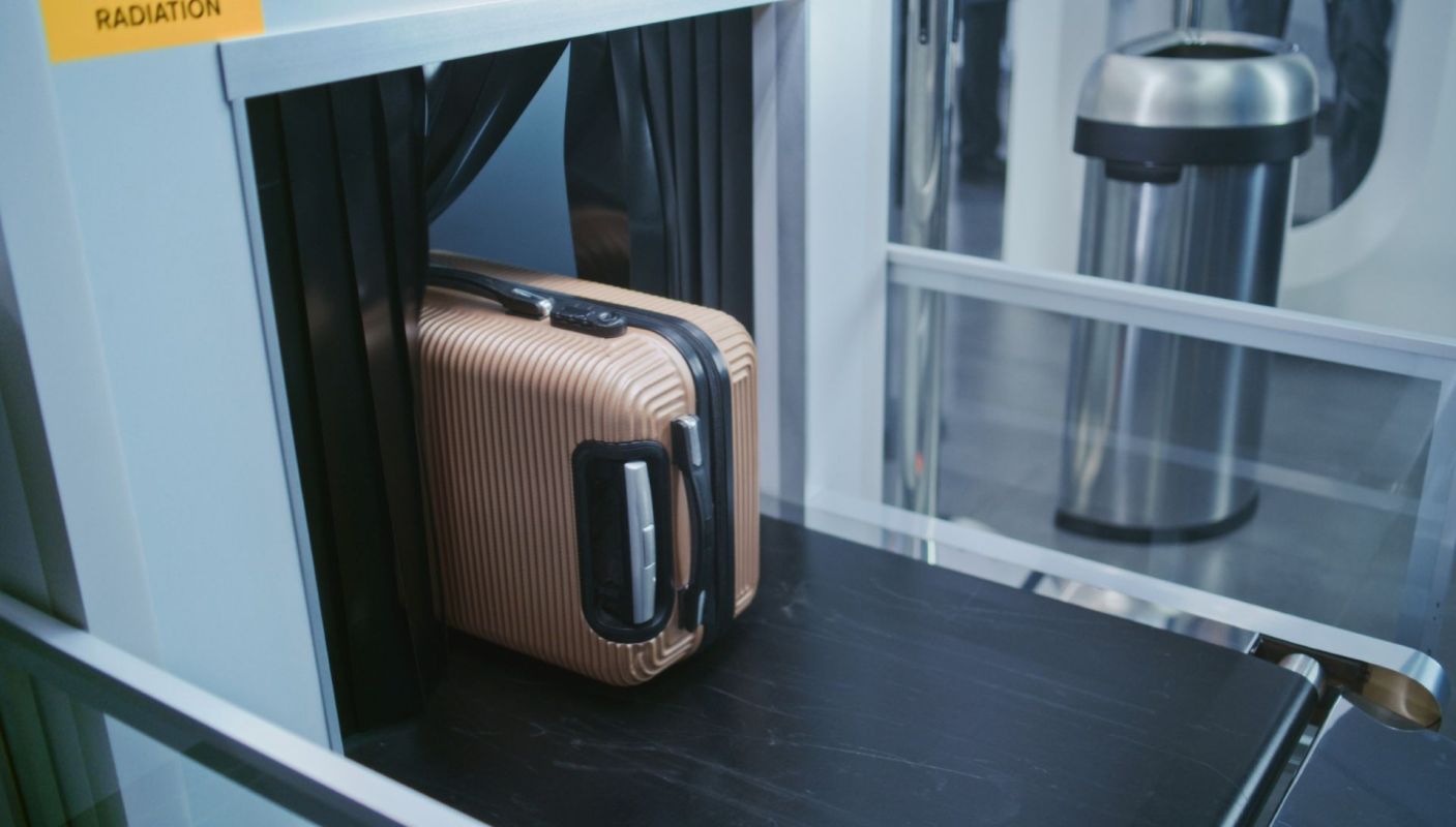 A brown striped suitcase placed on a conveyor belt at a security checkpoint.