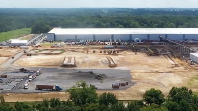 A construction site with heavy machinery and trucks near a large industrial building.