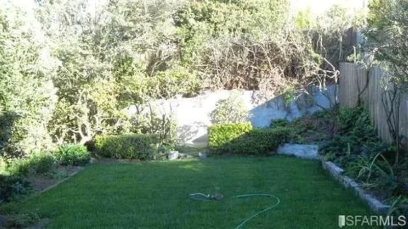 A garden predominantly featuring a lawn and bordered by plants and trees.