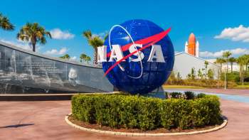 A large blue NASA globe sign with a space shuttle in the background, surrounded by palms and greenery.