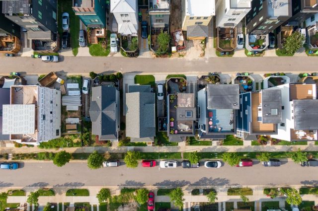 An overhead view of a residential street lined with various houses and parked cars.