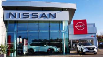 A Nissan dealership featuring large glass windows, new vehicles on display, and prominent branding.