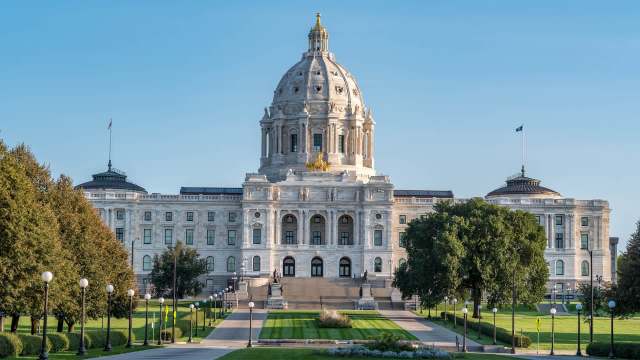 The Minnesota State Capitol building features a prominent dome and elegant stone architecture surrounded by landscaped grounds.