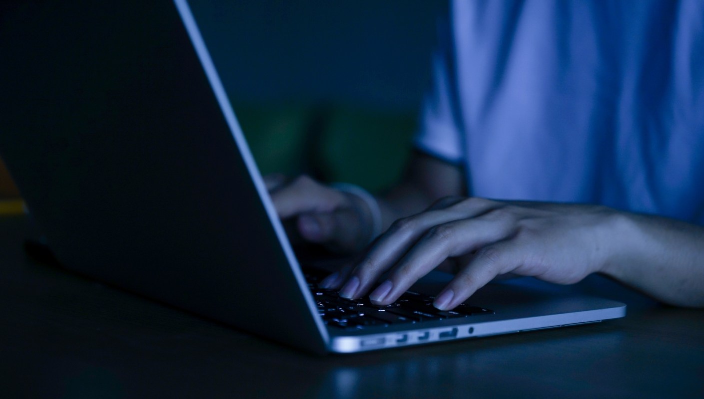 A person typing on a laptop in a dimly lit room.