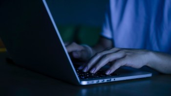 A person typing on a laptop in a dimly lit room.
