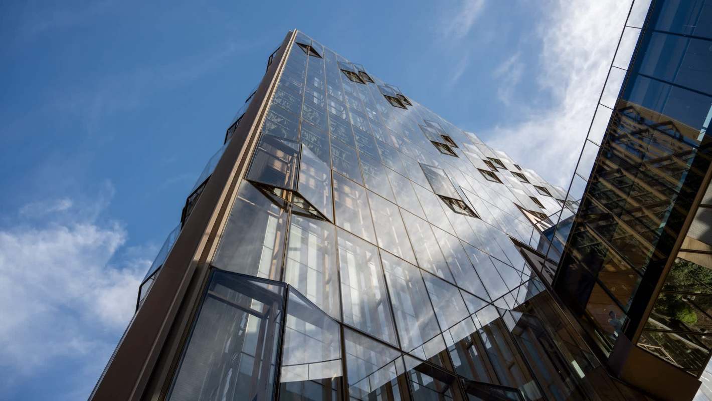 A modern glass building with a unique angular design reflecting the sky and surroundings.