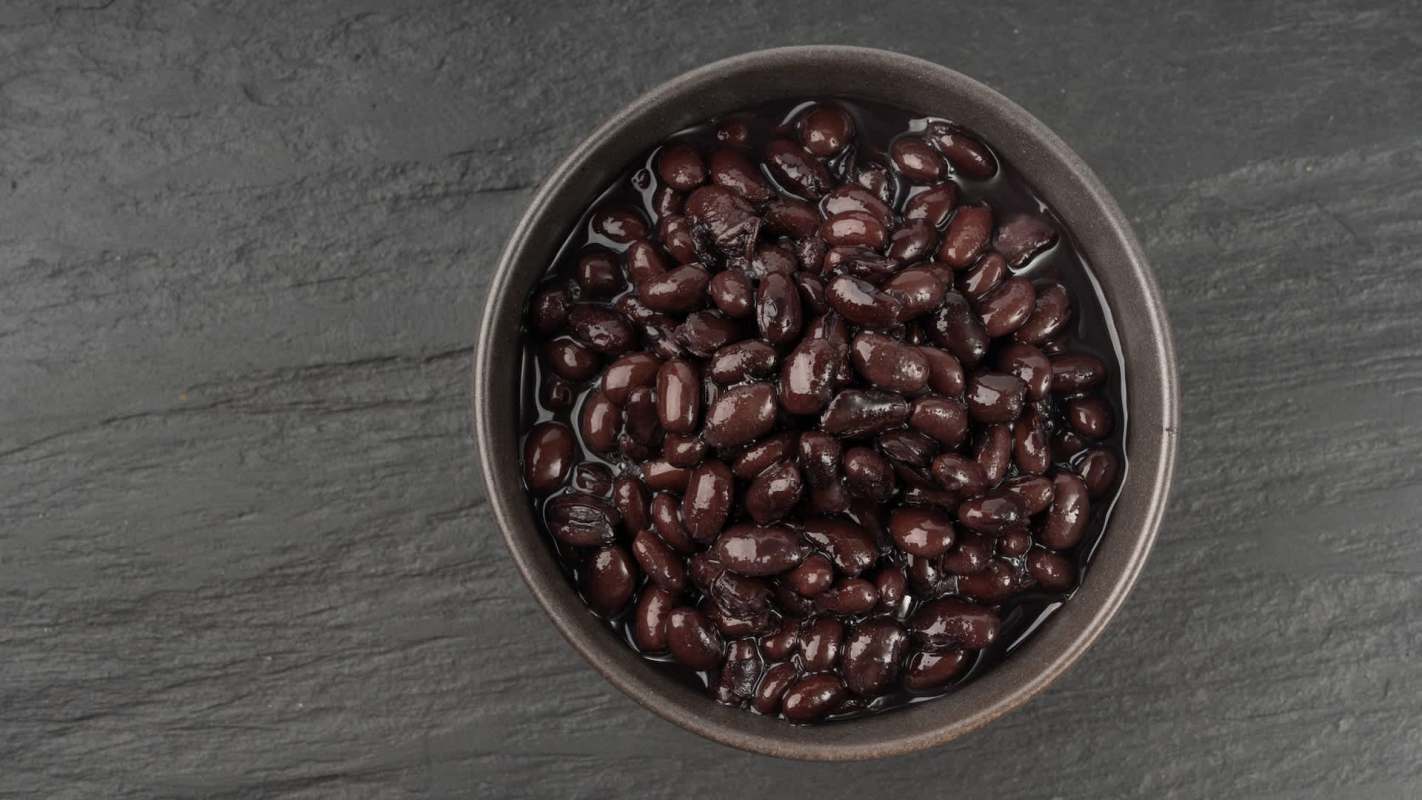 A bowl of black beans in liquid on a dark stone surface.